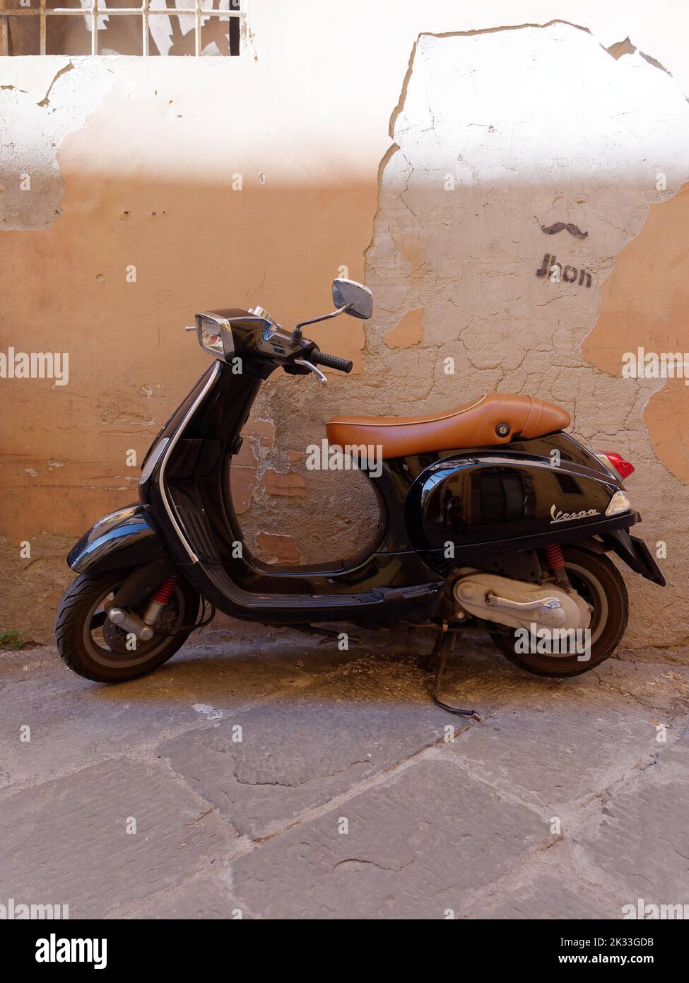 Vespa nera e un muro beige nella città di Lucca, Toscana, Italia Foto Stock