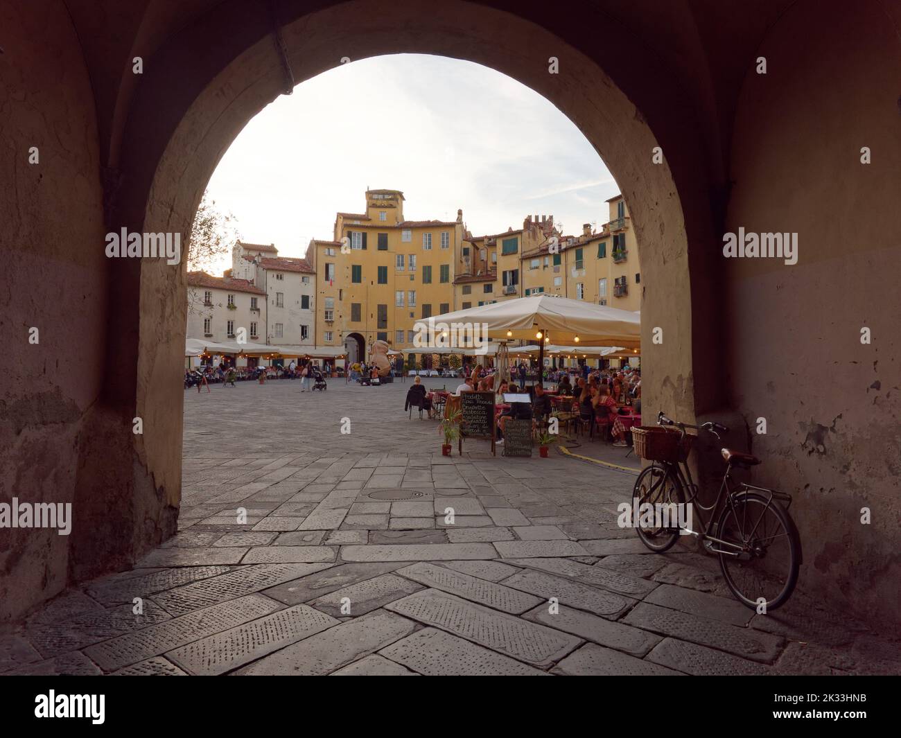La Piazza dell'Anfiteatro, a forma circolare, si vede attraverso un arco nel centro storico di Lucca, Toscana, Italia Foto Stock