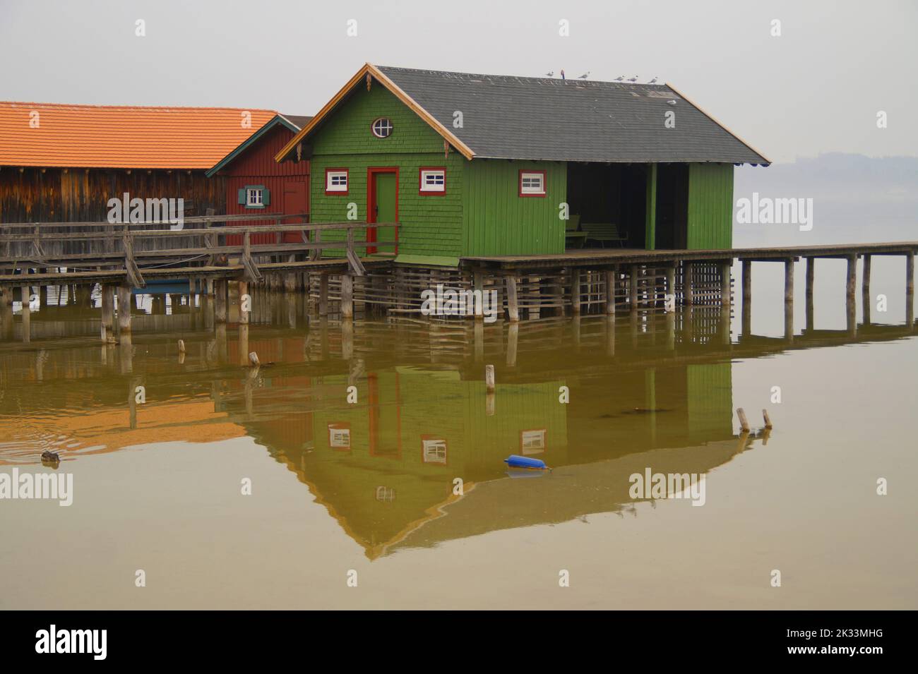 Lungo molo in legno che conduce alle colorate case delle barche sul lago Ammersee nel villaggio bavarese di Schondorf in una giornata buia e nebbiosa (Baviera, Germania) Foto Stock