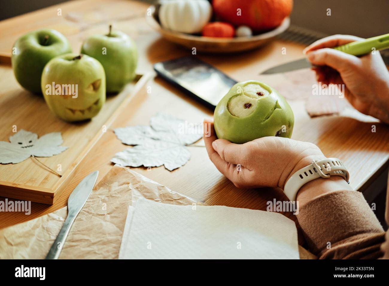 Idee di frutta fai da te di Halloween. Le mani femminili tagliano la mela verde di Halloween con la faccia creepy intagliata sul tavolo di legno nel paese. Spuntini salutari di Halloween Foto Stock