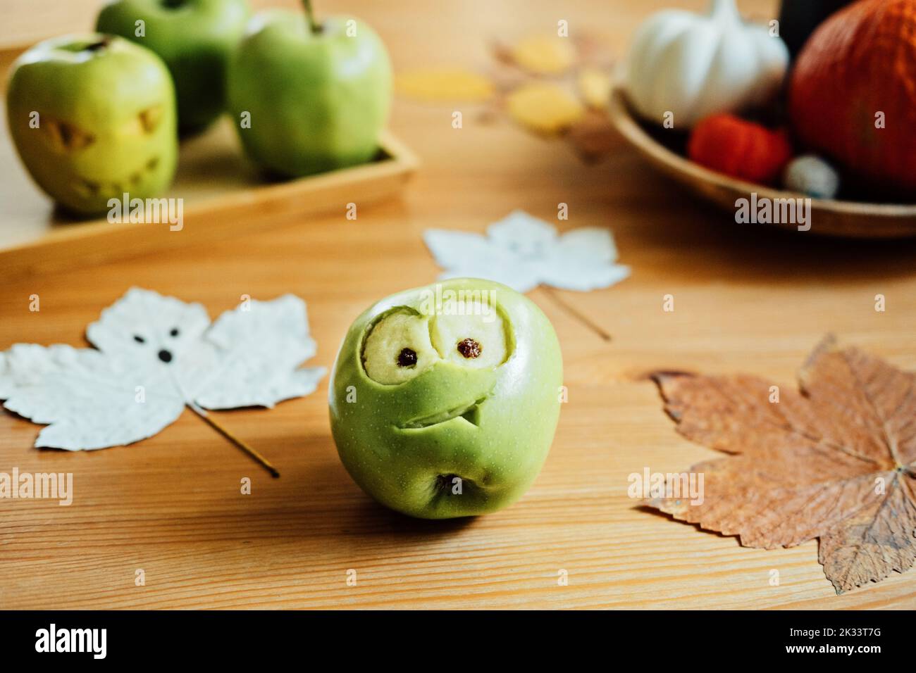 Idee frutto di Halloween. Mela verde di Halloween con faccia creepy intagliata sul tavolo di legno a casa. Spuntini salutari di Halloween Foto Stock