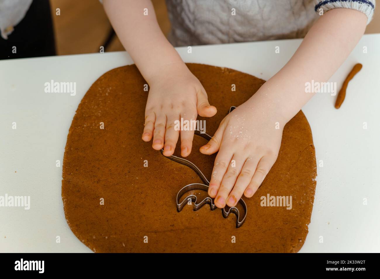 Le mani del ragazzo fanno il pan di zenzero a forma di capriolo di Natale dalla pasta sul tavolo da cucina, vista dall'alto Foto Stock