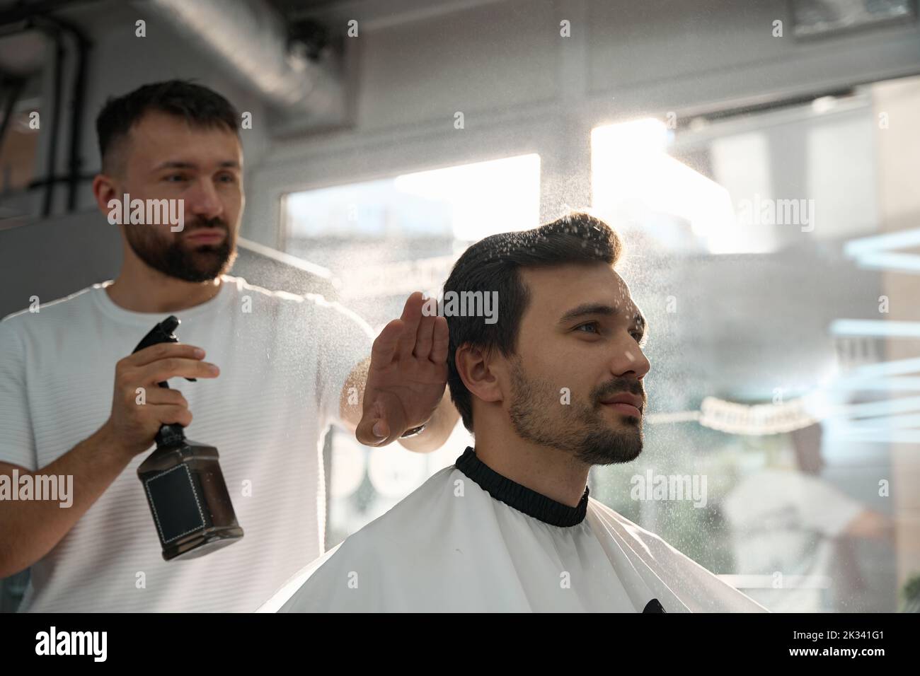 Barbiere professionale idratante i capelli del cliente prima di tagliarli Foto Stock