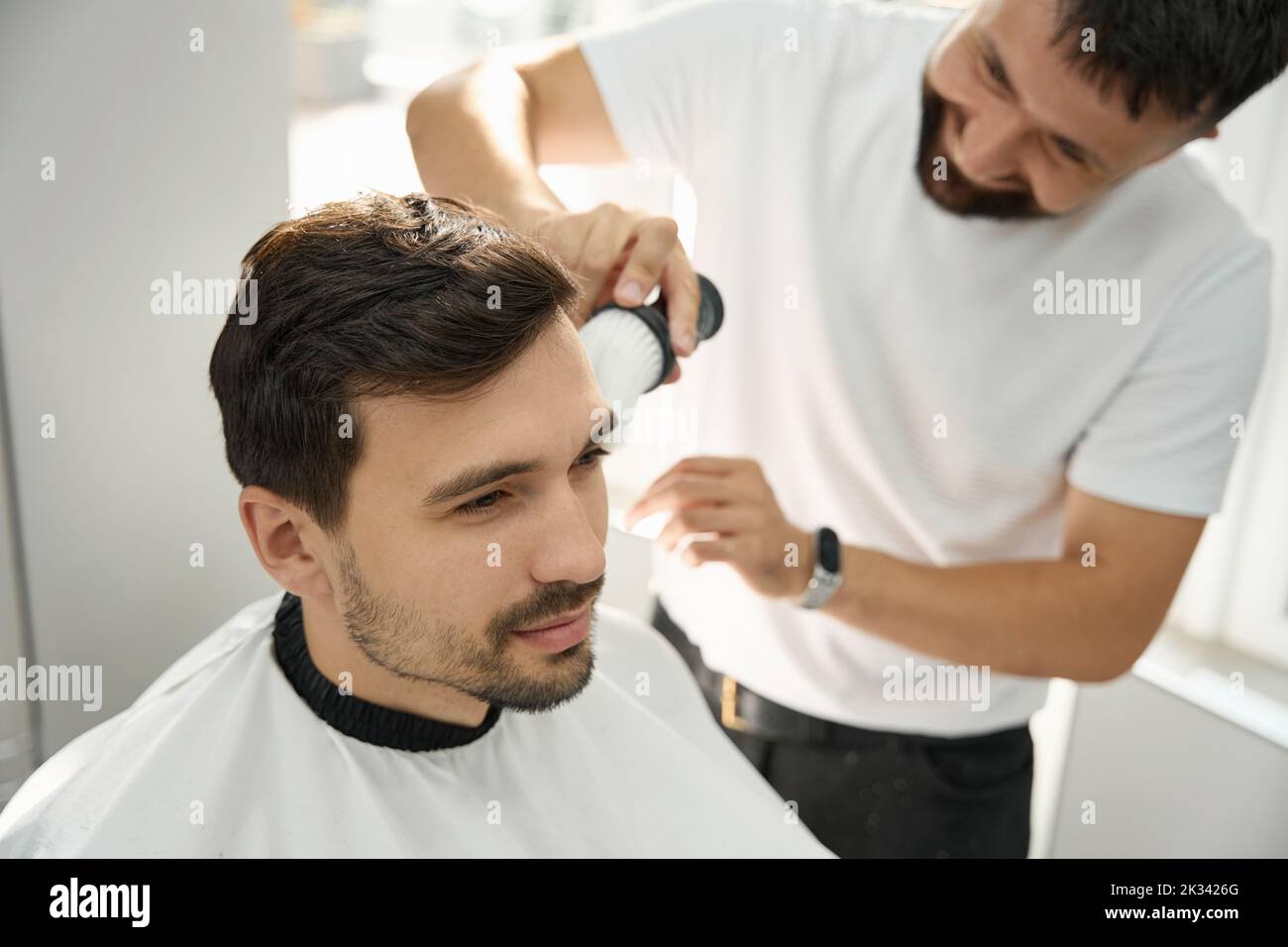 Cheerful hairstyle specialista spazzolare il viso dell'ospite dopo il taglio dei capelli Foto Stock