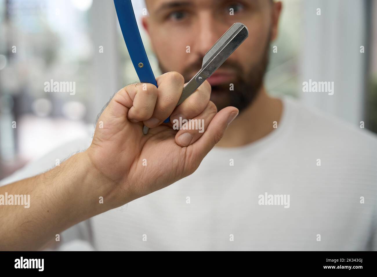 Un hair-groomer certificato ispeziona attentamente il suo strumento di rasatura principale Foto Stock
