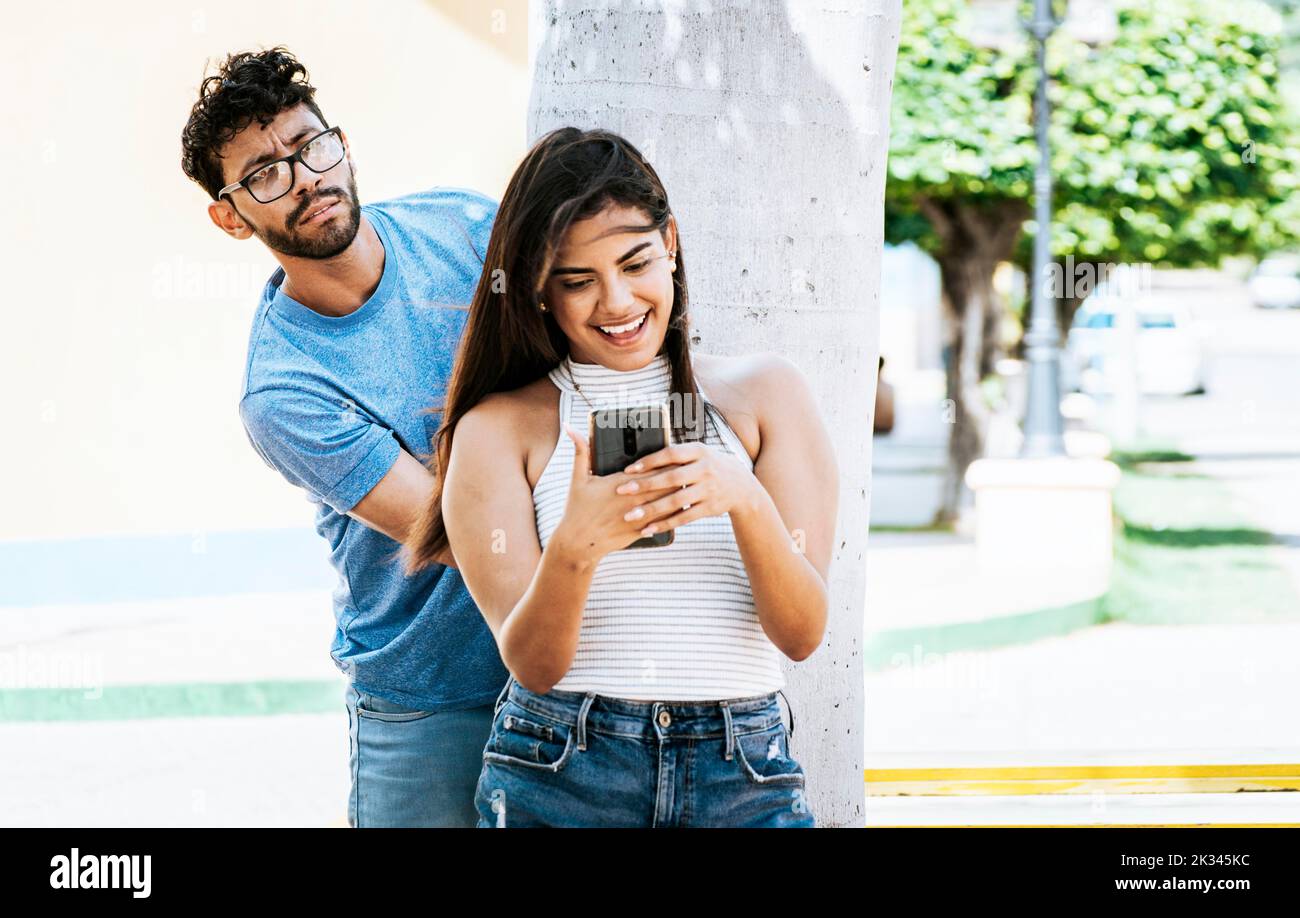 Il ragazzo geloso che spionava sul cellulare della sua ragazza nel parco, l'uomo geloso spionando sulla sua ragazza che SMS sul cellulare. Uomo sospetto Foto Stock