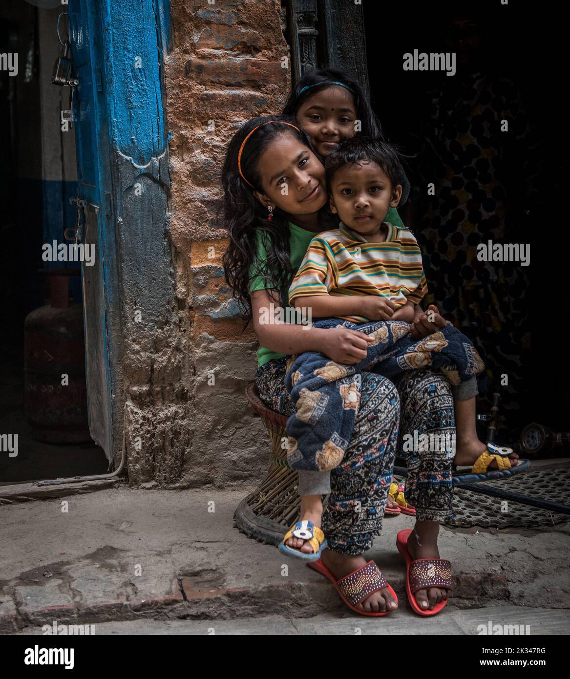 Tre bambini nepalesi dall'aspetto felice seduti fuori da una porta. Foto Stock