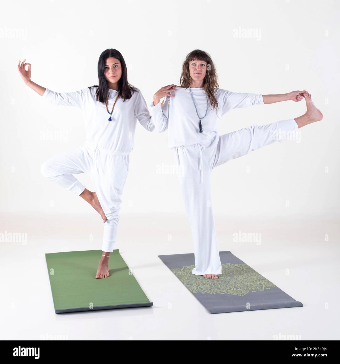 Due donne vestite di bianco che fanno pose yoga mentre guardano la fotocamera su sfondo bianco. Foto da studio Foto Stock