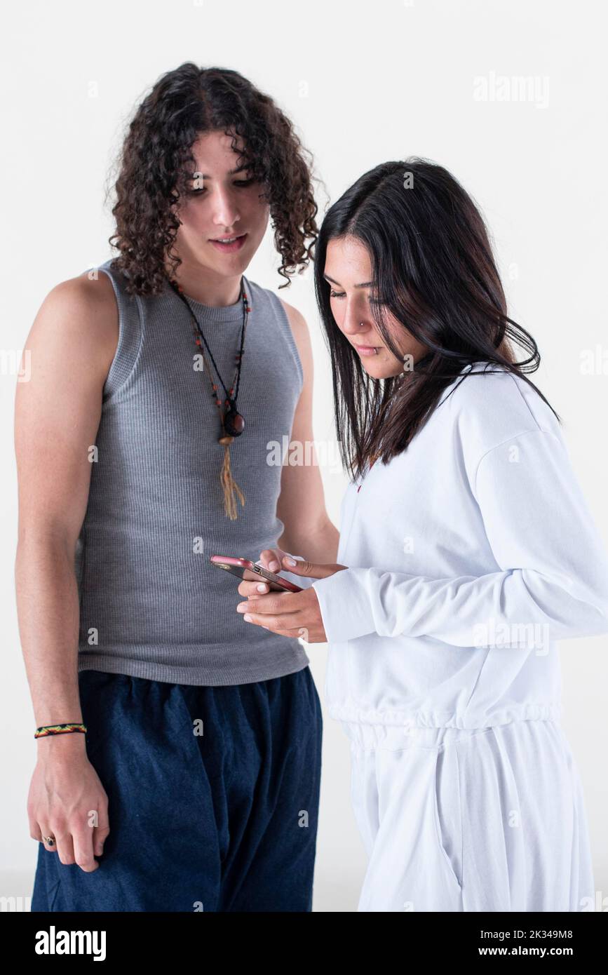 Ritratto di una giovane coppia vestita di abiti yoga guardando uno smartphone su sfondo bianco. Foto da studio Foto Stock