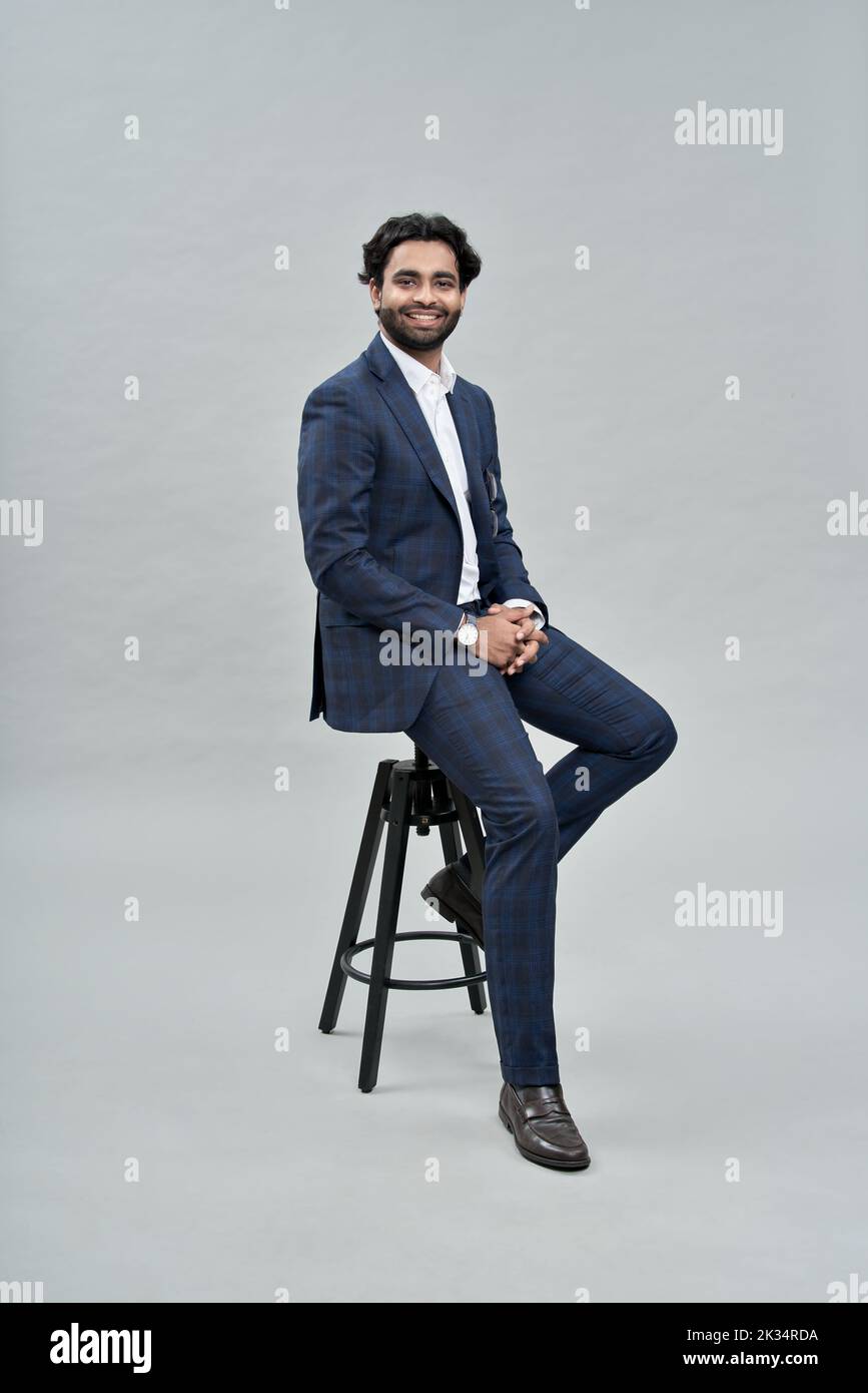 Felice riuscito giovane uomo arabo indiano di affari che indossa il vestito che siede sulla sedia Foto Stock