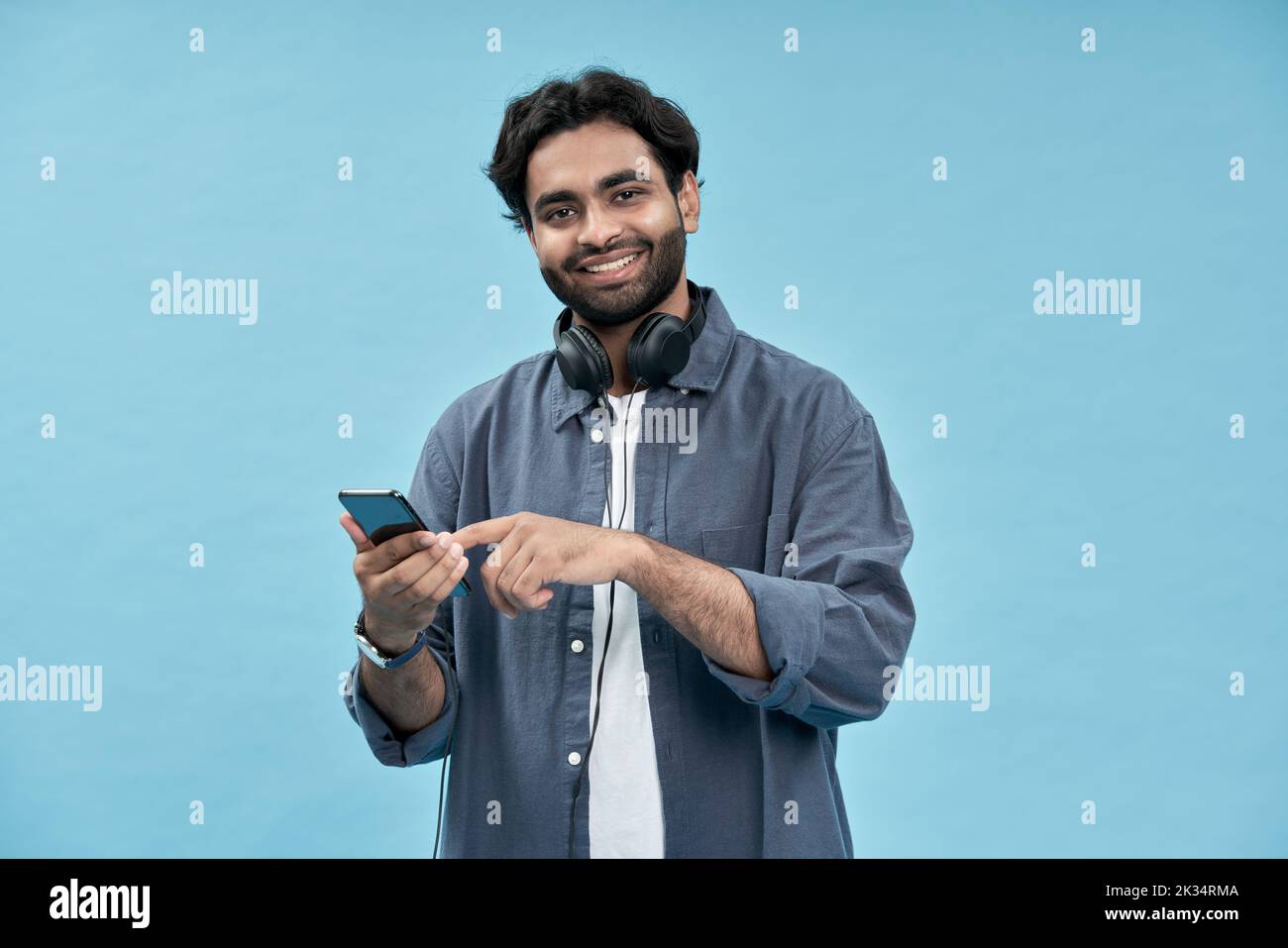 Felice uomo arabo studente utilizzando il telefono cellulare isolato su sfondo blu. Foto Stock