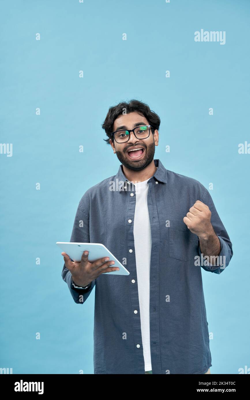 Entusiasta uomo arabo vincitore alzando ostinante tablet isolato su blu. Foto Stock