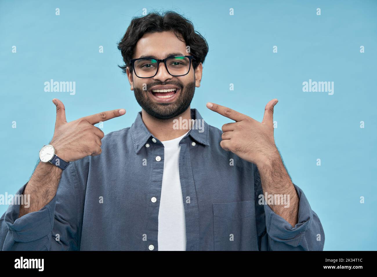 Uomo arabo felice che punta le dita a denti bianchi sani isolati sul blu. Foto Stock