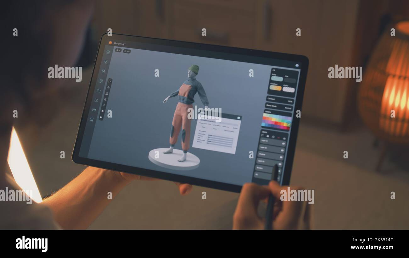 Designer 3D maschile che crea design di abiti in un'applicazione di modellazione 3D utilizzando computer tablet e matita digitale mentre lavora in remoto su un progetto freelance Foto Stock