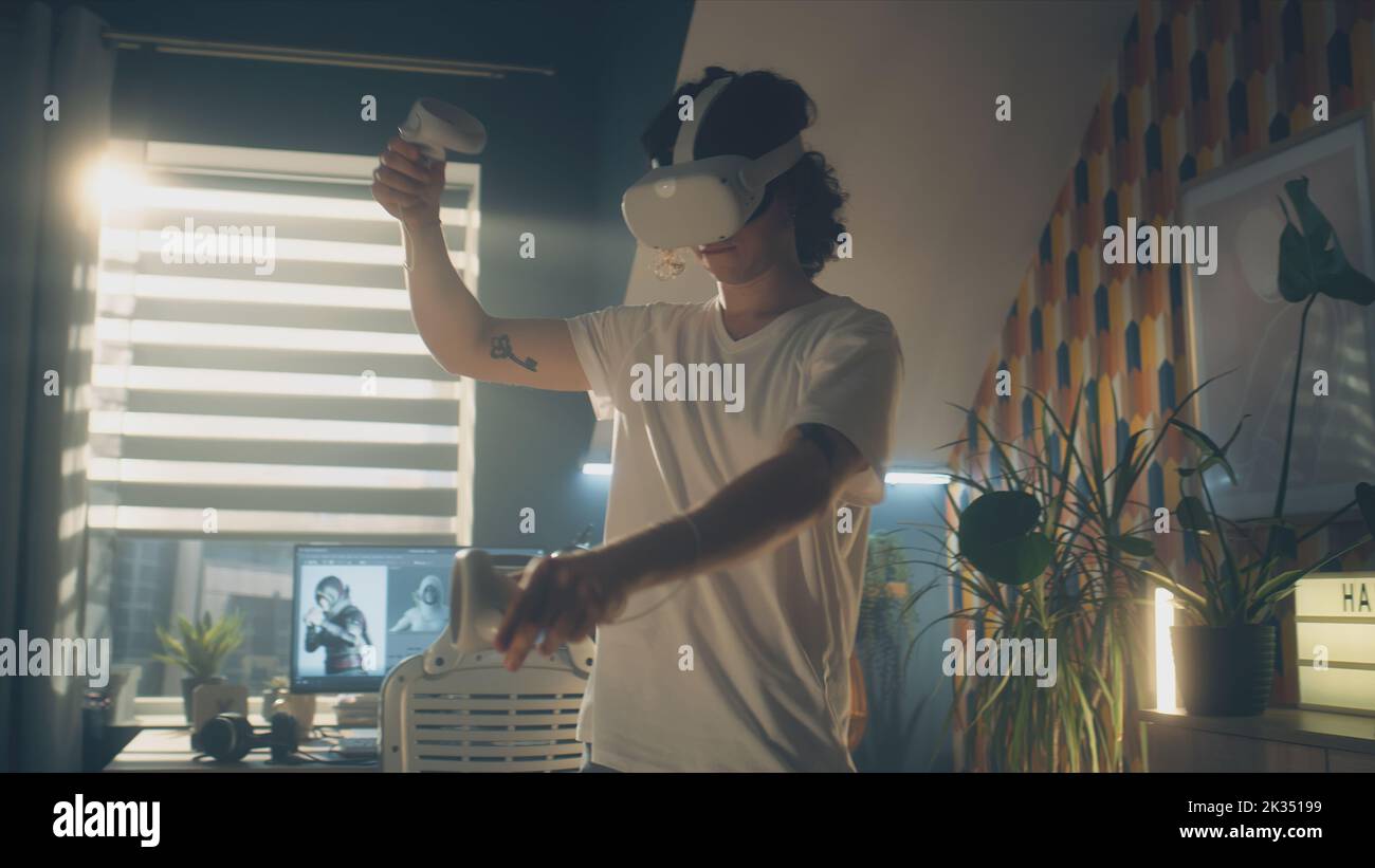 Uomo che prova e gioca ai videogame utilizzando occhiali di protezione VR e controller wireless mentre passa il tempo libero a casa. Dispositivo per realtà virtuale. Cyberspazio e metaverse Foto Stock