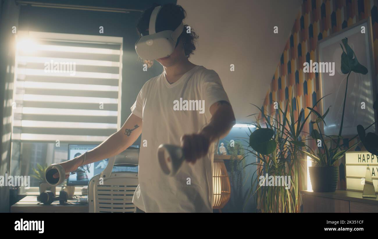 Uomo che prova e gioca ai videogame utilizzando occhiali di protezione VR e controller wireless mentre passa il tempo libero a casa. Dispositivo per realtà virtuale. Cyberspazio e metaverse Foto Stock