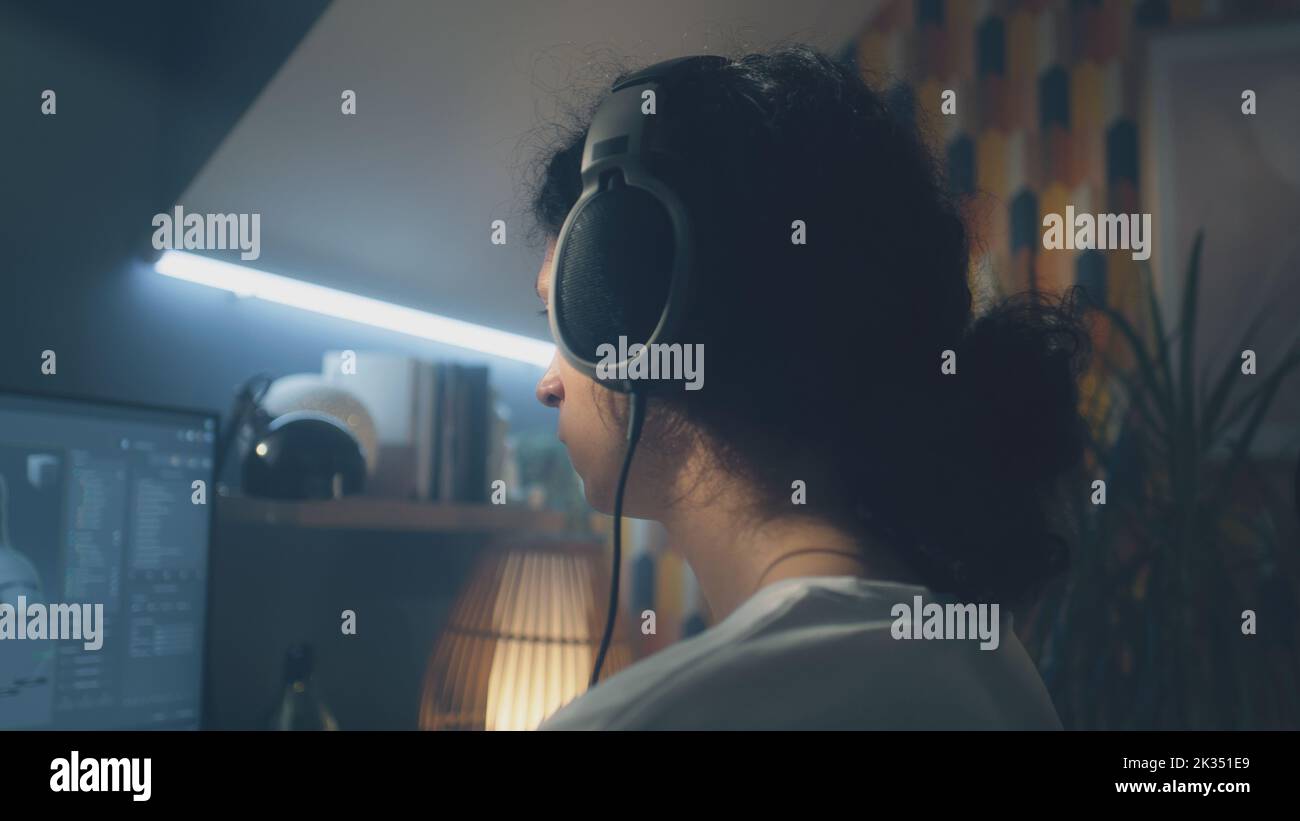 Uomo in cuffia che naviga su Internet e sui social network sul computer di casa di notte e ascolta musica o lavora online da freelance Foto Stock