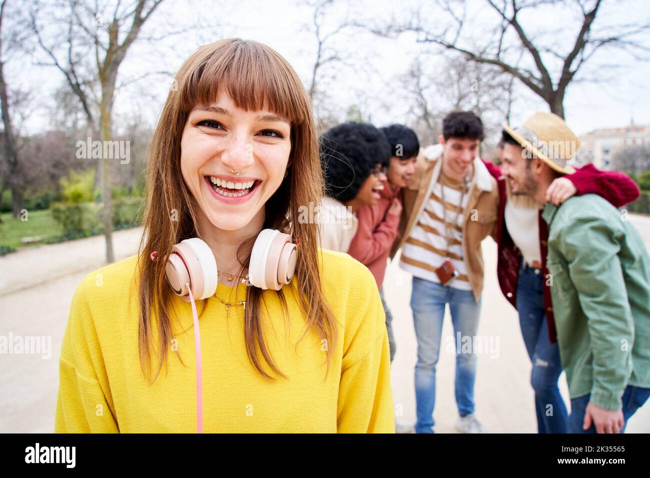 Giovane ragazza sorridente che guarda la fotocamera all'aperto con un gruppo di amici. Persone felici divertirsi insieme concentrarsi su una bella giovane donna. Università Foto Stock