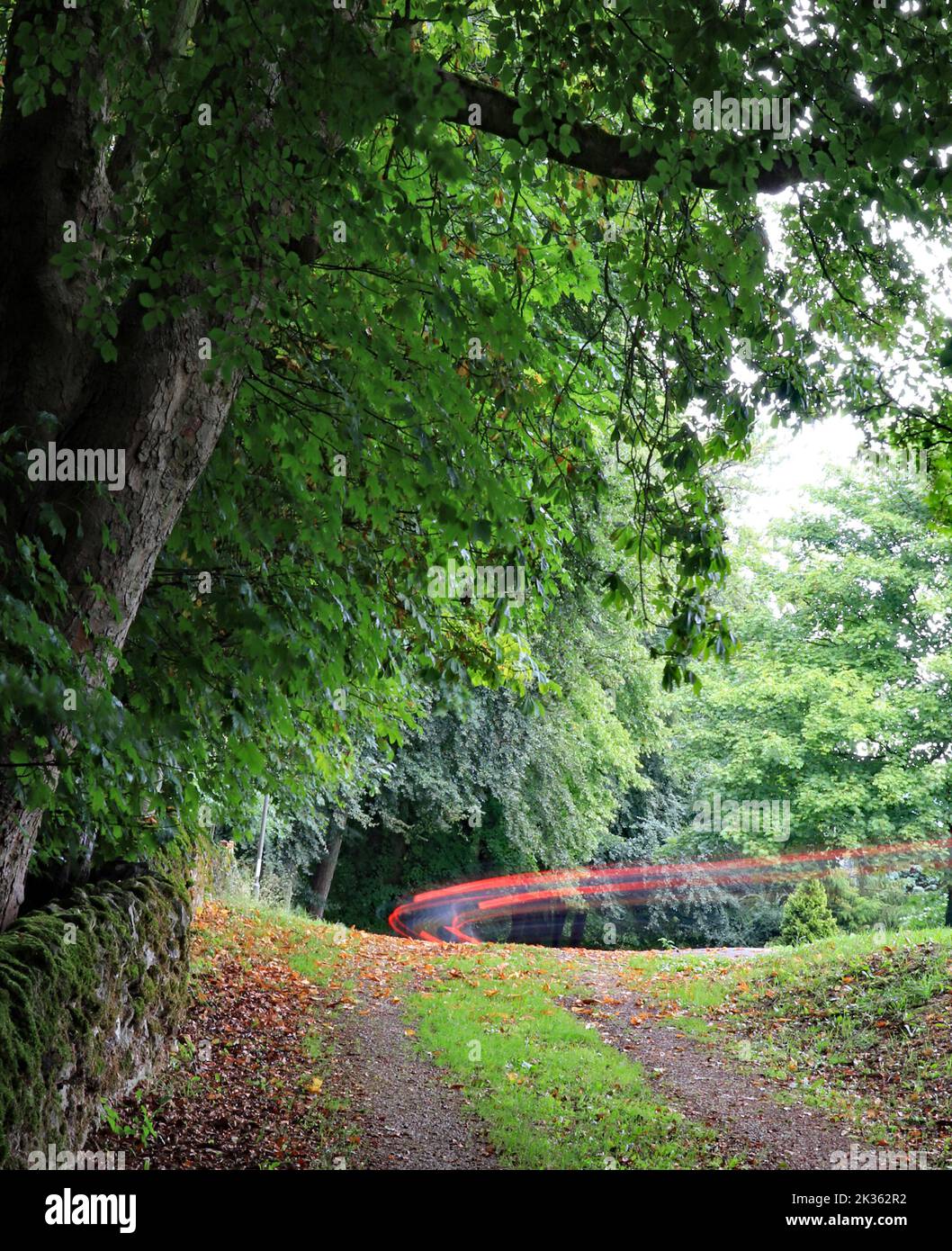 In cima alla Cisgiordania, a Winster, le luci di stop di un’auto lasciano una bella curva di luce rossa in una giornata di noia mentre sparisce lungo la riva. Foto Stock