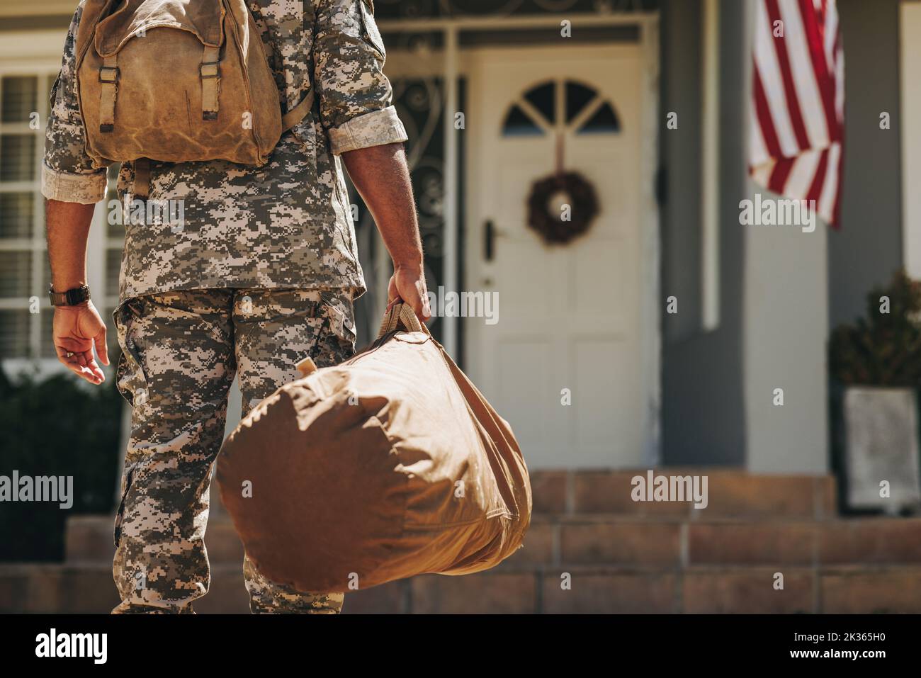 Soldato irriconoscibile che si trova davanti a casa sua con i bagagli. Vista posteriore di un serviceman americano patriottico che torna a casa dopo aver servito il suo Foto Stock