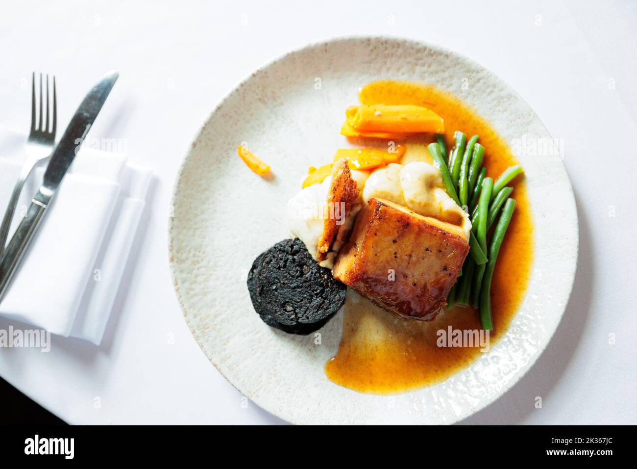 Maiale arrosto lento in uno smalto di miele e soia con budino nero, crackling e salvia Foto Stock
