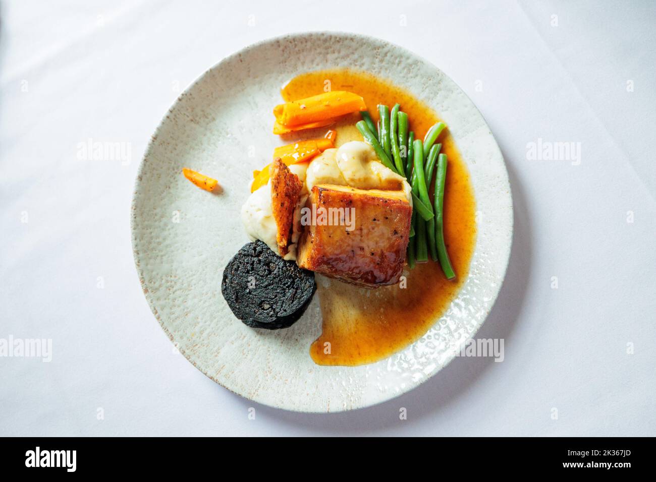 Maiale arrosto lento in uno smalto di miele e soia con budino nero, crackling e salvia Foto Stock