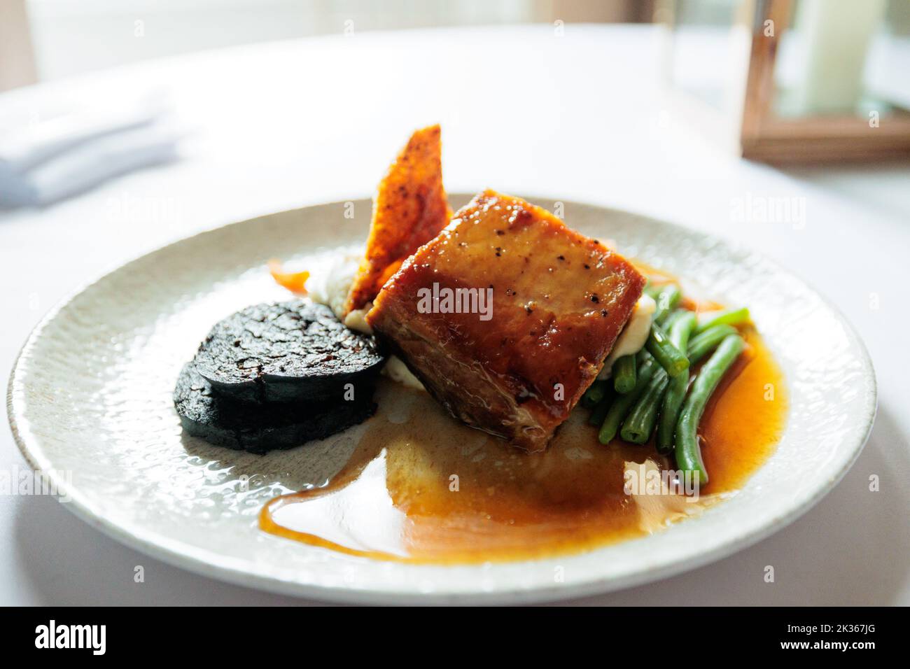 Maiale arrosto lento in uno smalto di miele e soia con budino nero, crackling e salvia Foto Stock