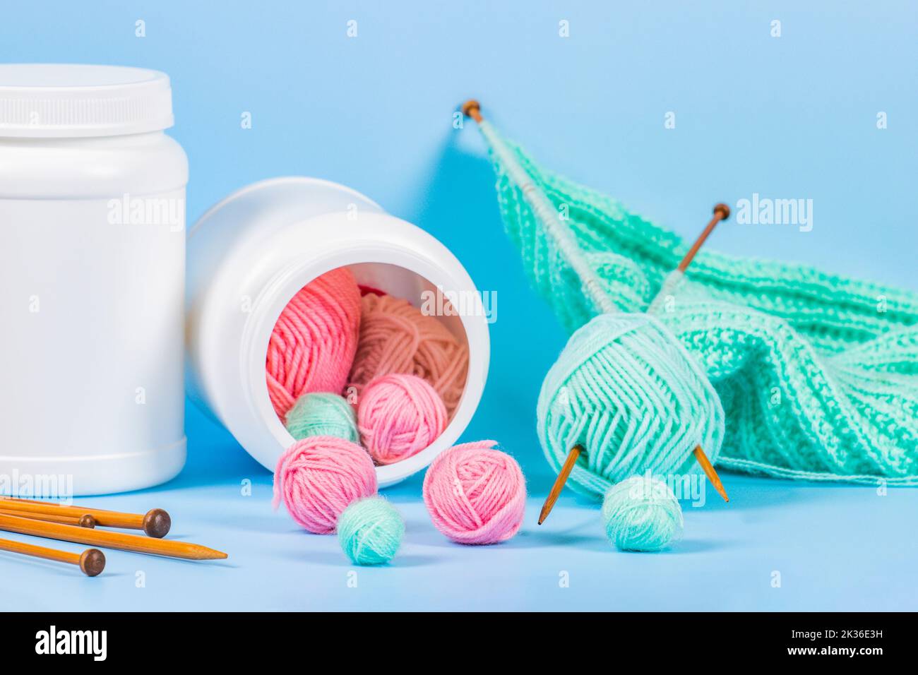 Lavorare a maglia come terapia. Palle di filettatura come supplementi versati fuori della bottiglia. Aghi in legno con maglieria su sfondo azzurro. La salute della lavorazione a maglia Foto Stock