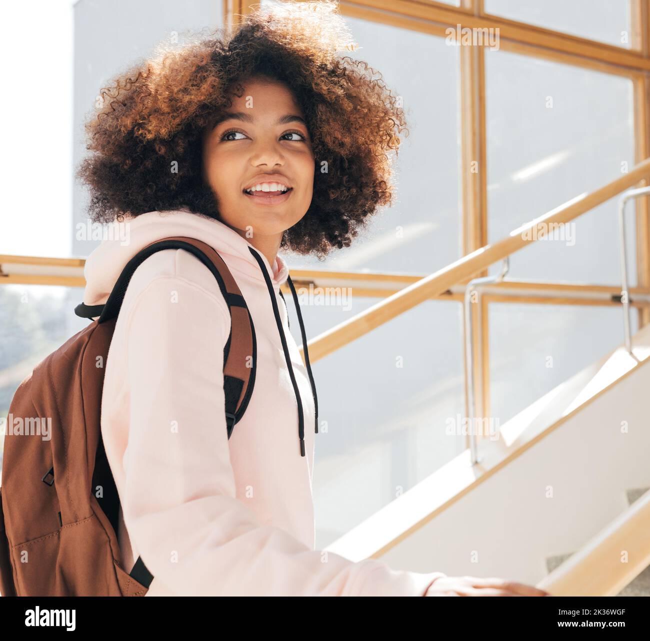 Ragazza felice con i capelli ricci che guardano indietro mentre salendo sulle scale della scuola Foto Stock