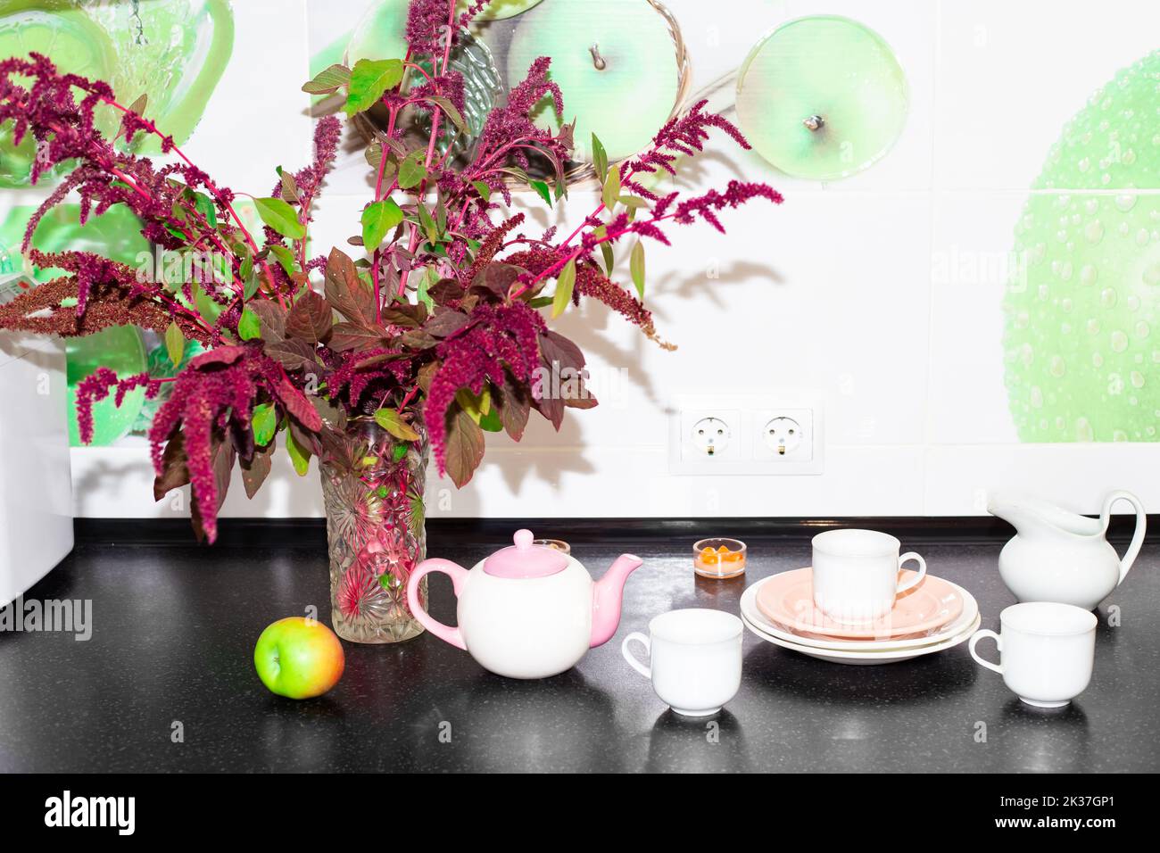 Fiori di Borgogna di amaranto vegetale in un vaso su un piano di lavoro nero cucina con piatti. Decorazione della cucina. Foto Stock