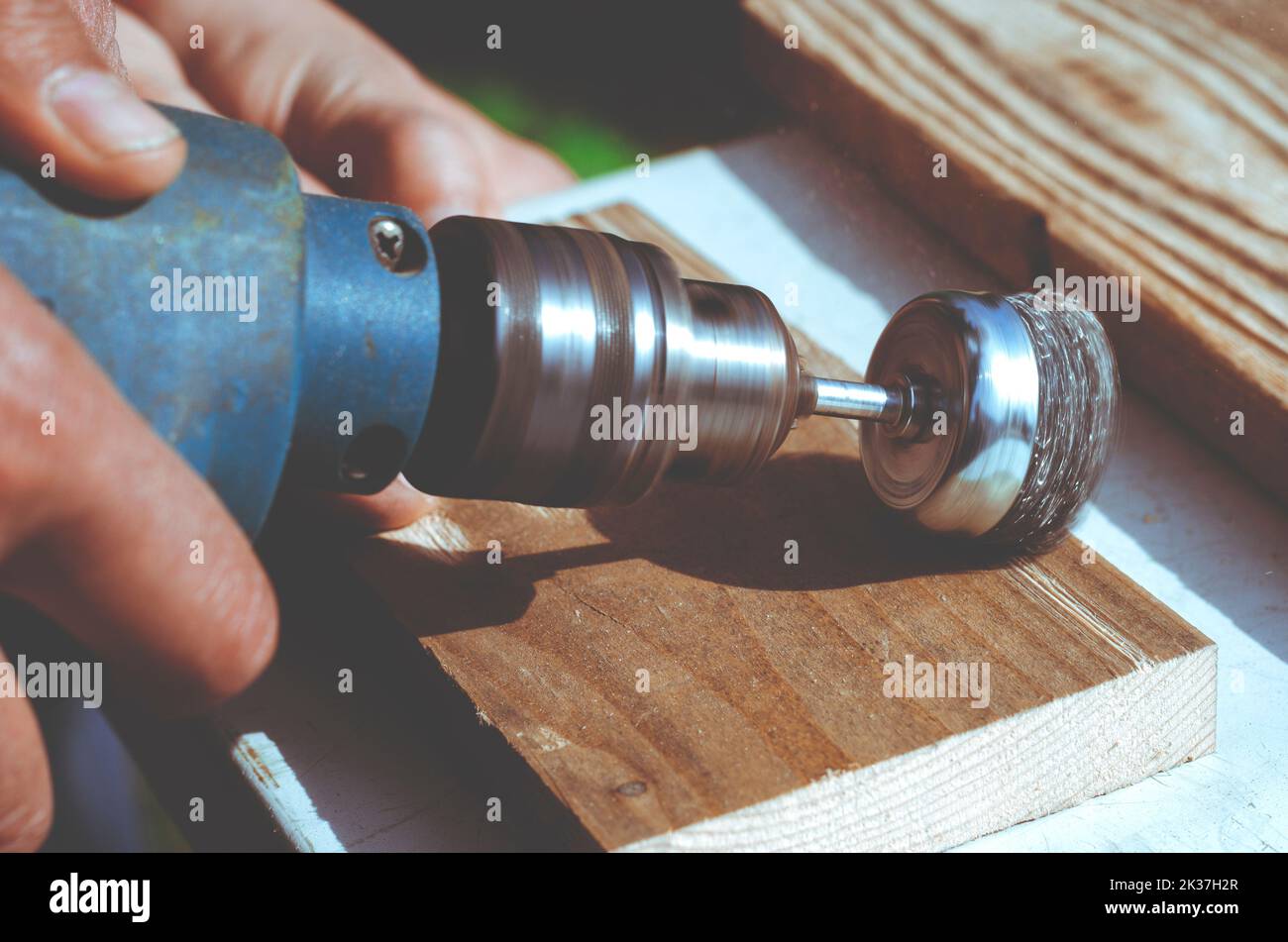 Mani uomo elettrico con spazzola rotante disco metallico levigazione di un pezzo di legno. Macchine per la lavorazione del legno all'esterno. Foto Stock