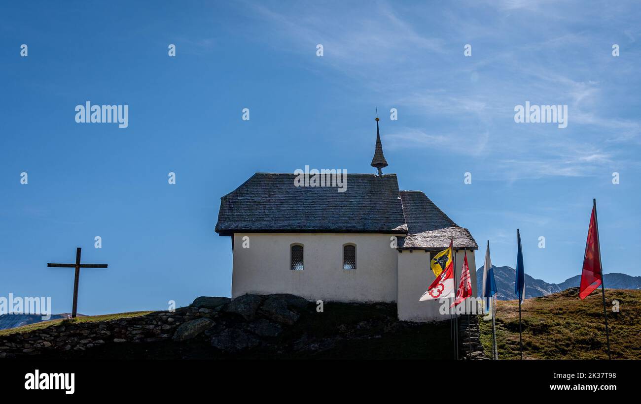 Paesaggio di chiesa e montagne. Chiesa svizzera di Bettmeralp con bandiere cantonali svizzere. Ambiente tranquillo. Foto Stock