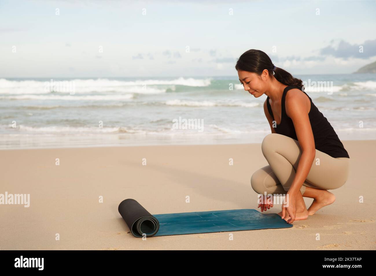 donna che sparge materassino yoga sulla spiaggia mattina praticare yoga al mare di spiaggia, giovane donna esercizi o meditare in spiaggia fare yoga Foto Stock
