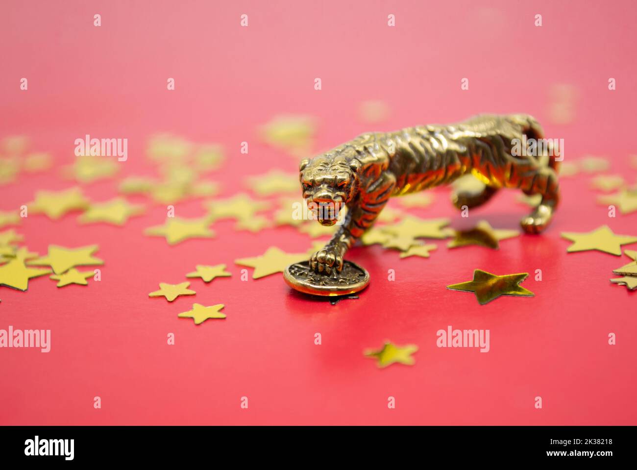 Figura bronzea di una tigre con moneta su sfondo rosso con stelle dorate, copia spazio. Auguri di buona fortuna, ricchezza. Foto Stock