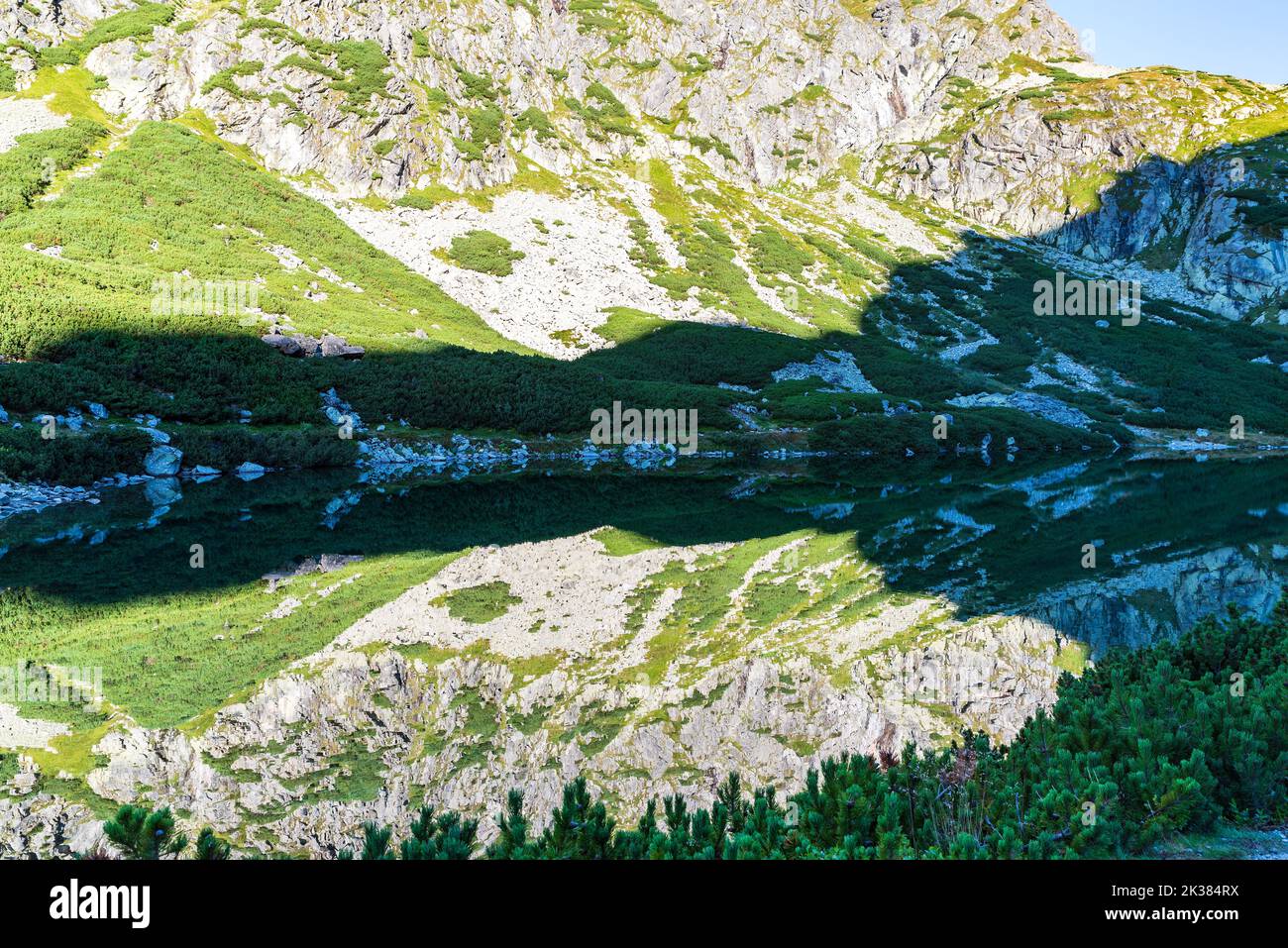 Colline rocciose che si specchiano sul terreno d'acqua del lago di Vericke pleso negli alti Tatra in Slovacchia durante l'autunno mattina con cielo limpido Foto Stock