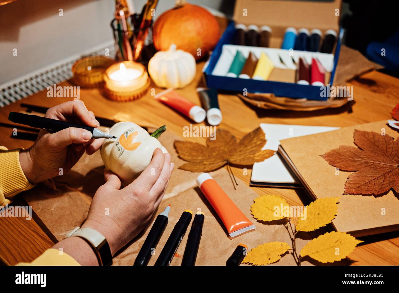 Autunno zucche artigianato. Artigianato autunnale fai da te per adulti. Le mani femminili disegnano i motivi sulla zucca bianca contro lo sfondo di decorazione autunnale sul tavolo a casa Foto Stock