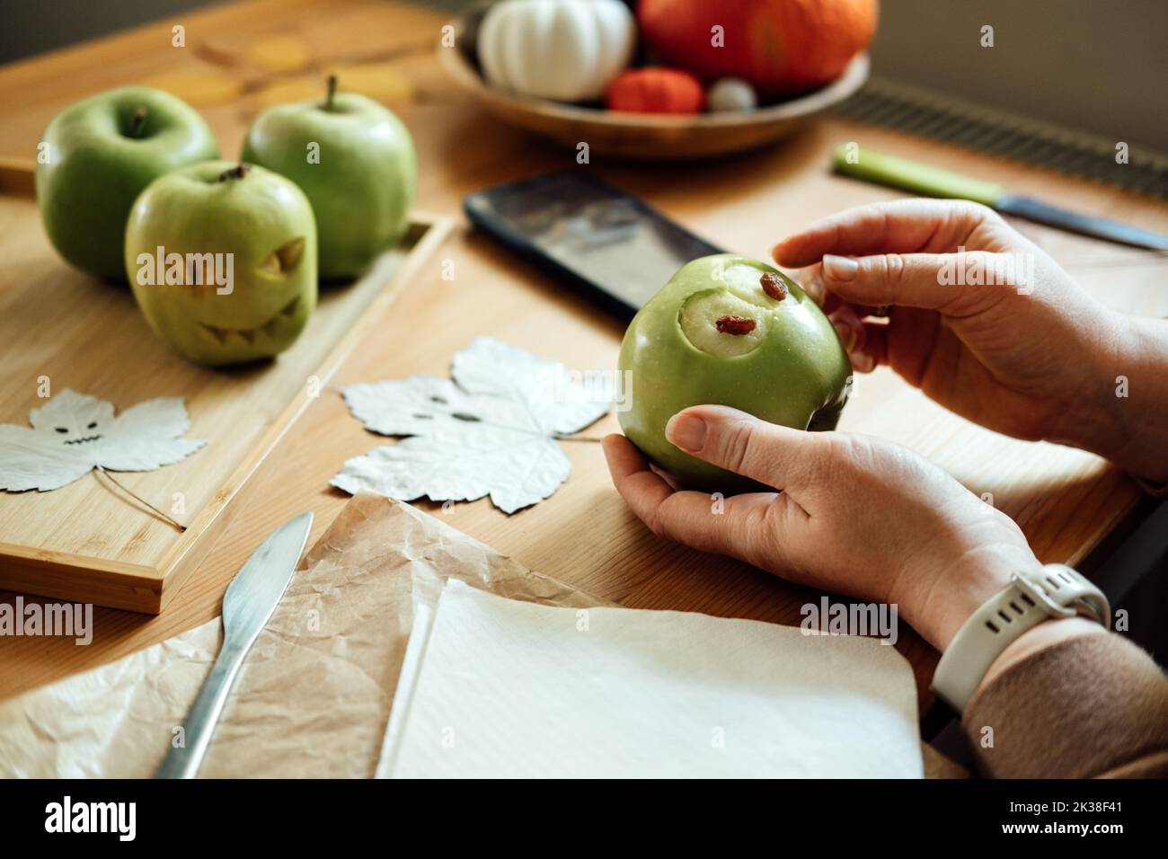 Idee di frutta fai da te di Halloween. Le mani femminili tagliano la mela verde di Halloween con la faccia creepy intagliata sul tavolo di legno nel paese. Spuntini salutari di Halloween Foto Stock
