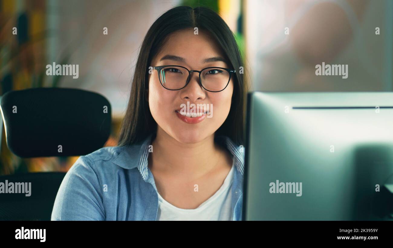 Donna asiatica in occhiali guardando lo schermo del computer mentre si lavora su progetti di modellazione 3D o di progettazione a distanza da casa o navigare in Internet in tempo libero. Freelance Foto Stock