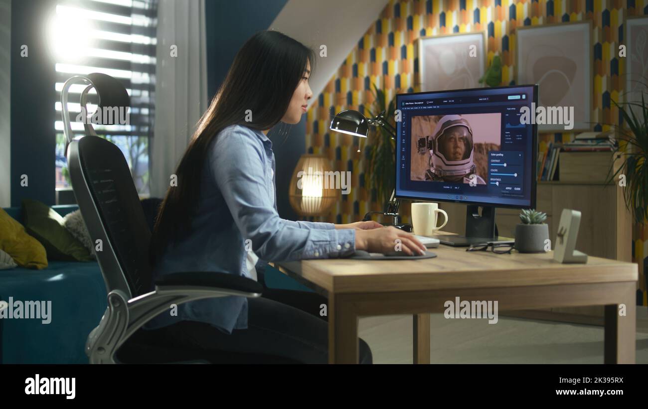 Freelancer asiatico femmina che modifica l'immagine con astronauta sul computer in photoshop mentre lavora in remoto da casa ufficio Foto Stock