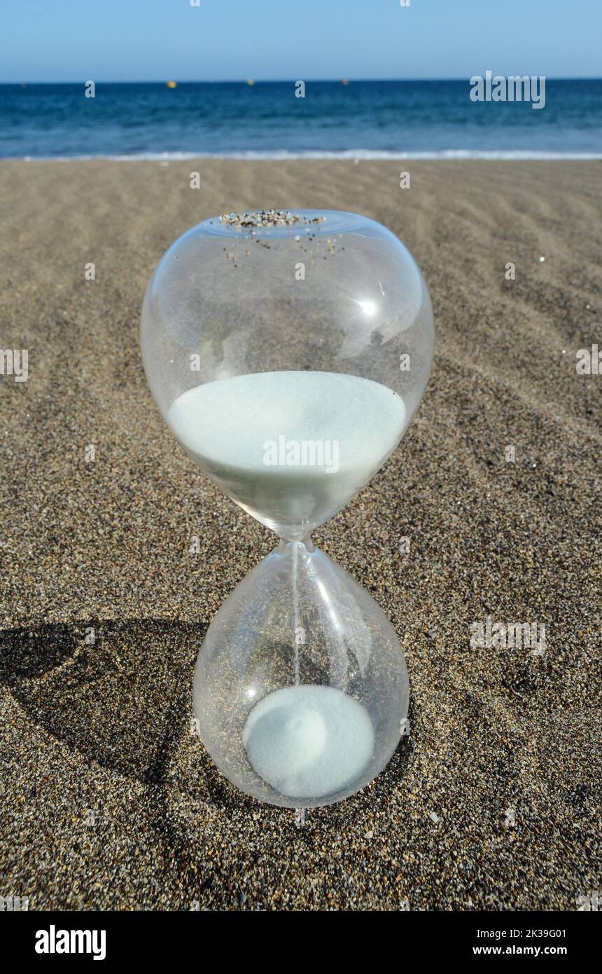 Un primo piano di una clessidra posta sulla spiaggia con il mare blu sullo sfondo Foto Stock