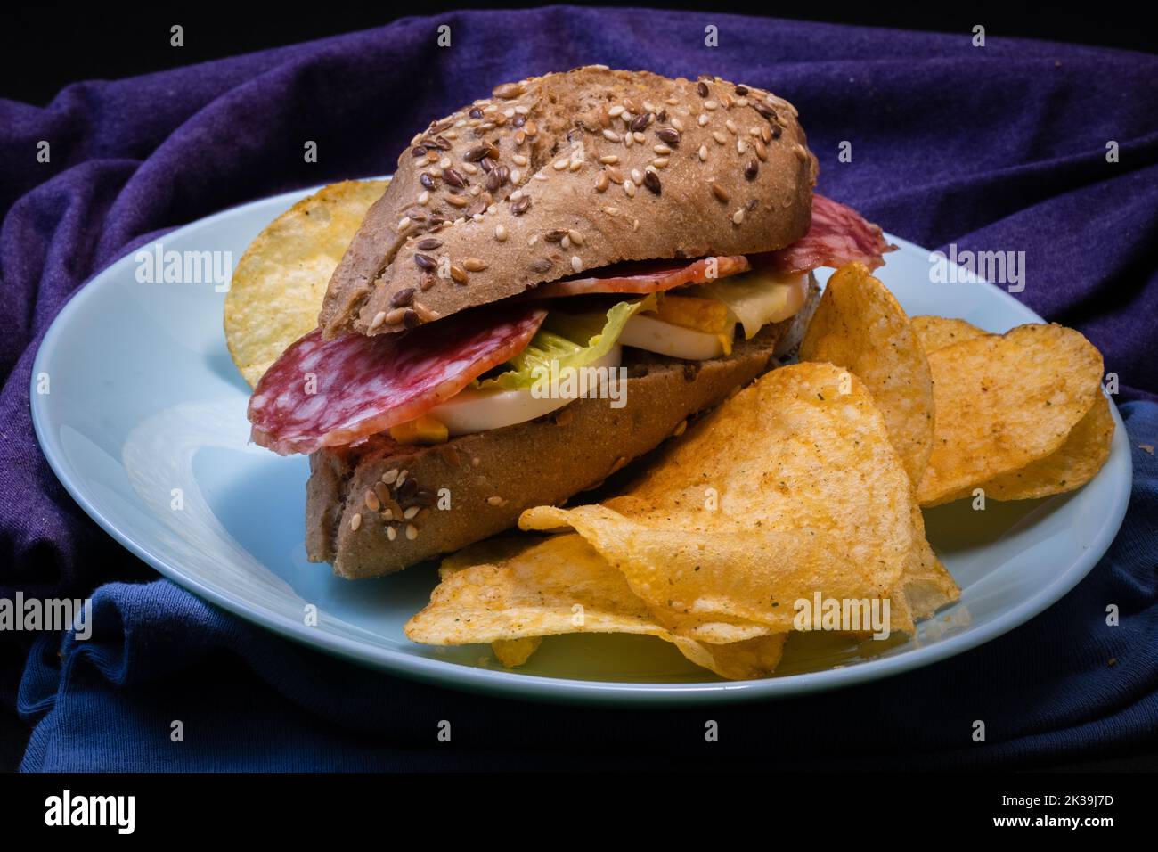 Sandwich con un panino rustico, salame, patatine fritte, insalata, sottaceti, cipolla e un uovo bollito su un piatto blu Foto Stock