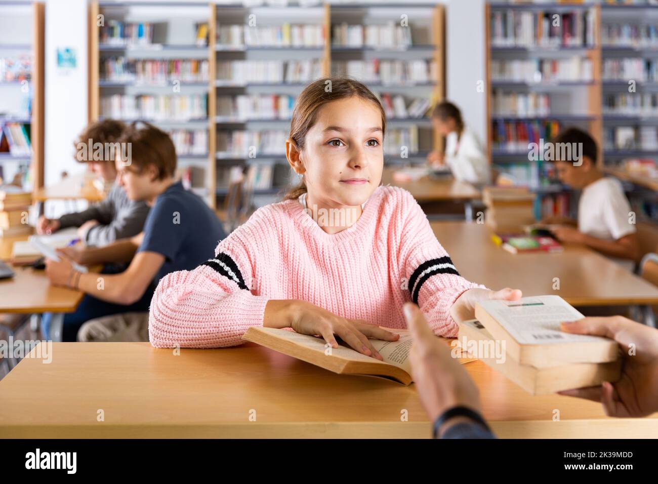 La ragazza preseen dà i libri letti al bibliotecario della biblioteca scolastica Foto Stock