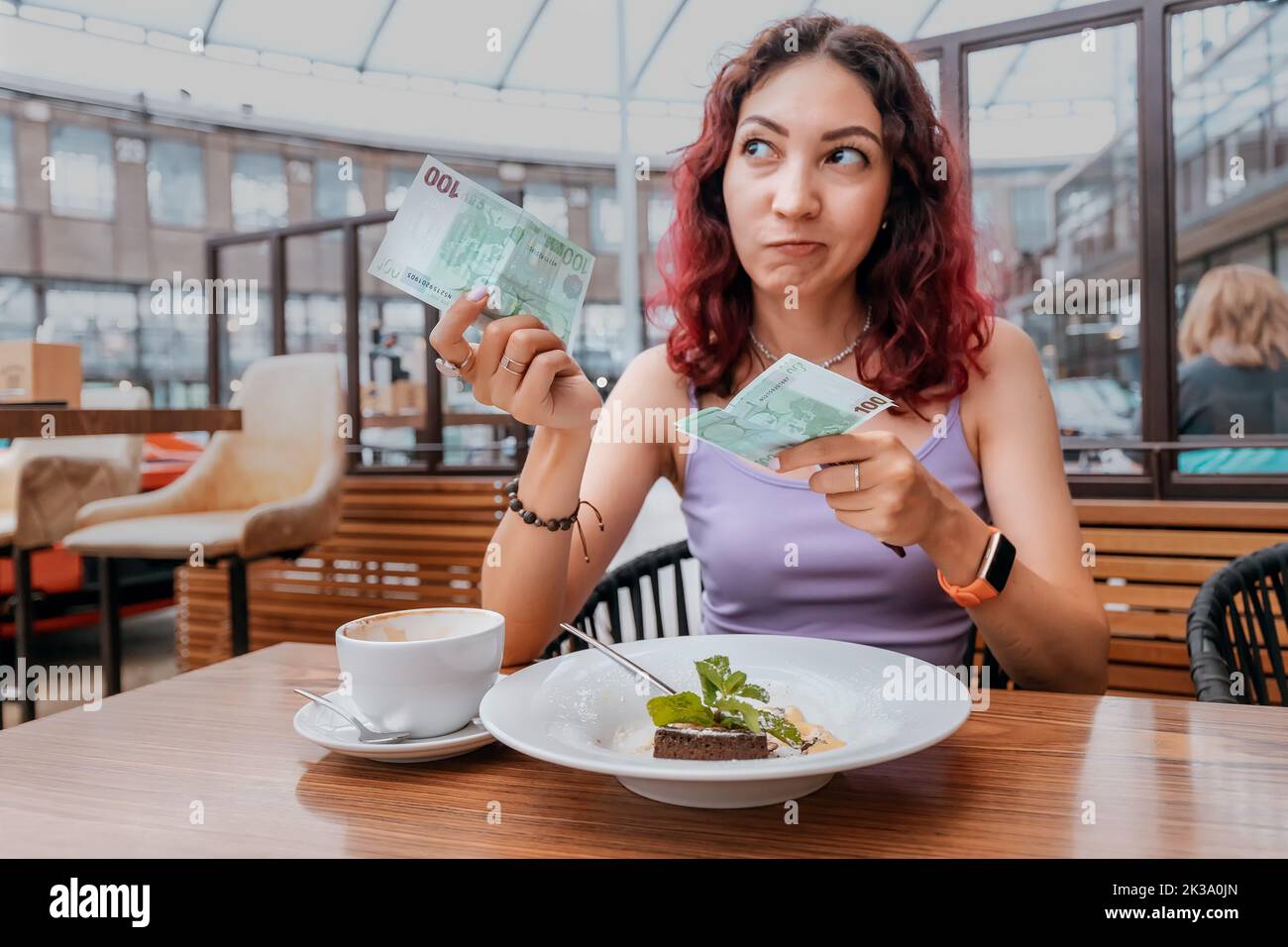 Una ragazza frustrato paga per il suo dessert in una caffetteria con una fattura dell'euro. Il concetto di inflazione e un forte aumento dei prezzi Foto Stock