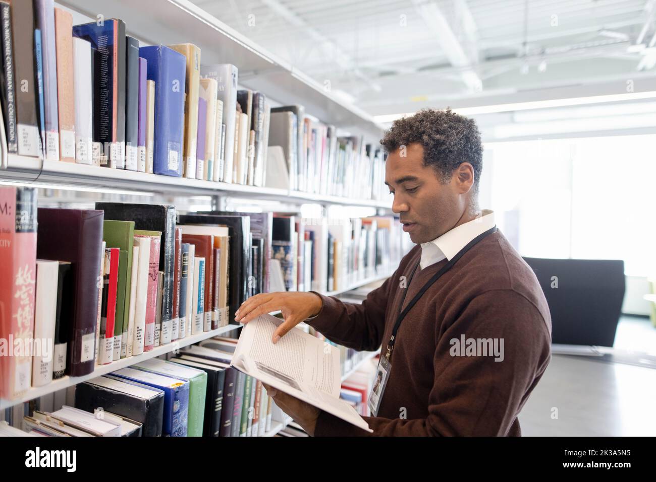 Professore universitario maschio con libro di testo alla libreria Foto Stock