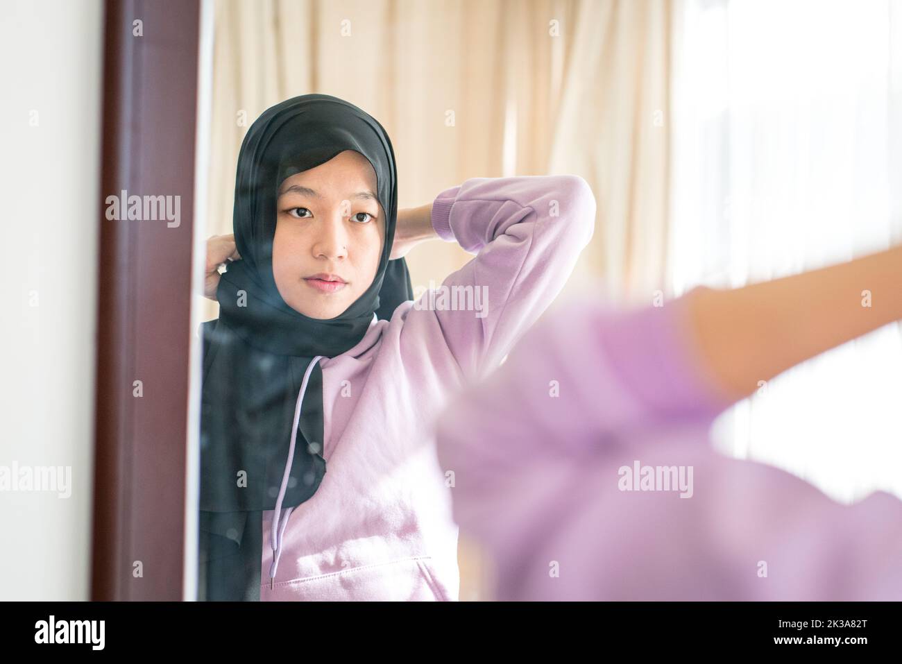 Riflessione su uno specchio da parete di una donna musulmana che indossa la sua foulard testa. Foto Stock