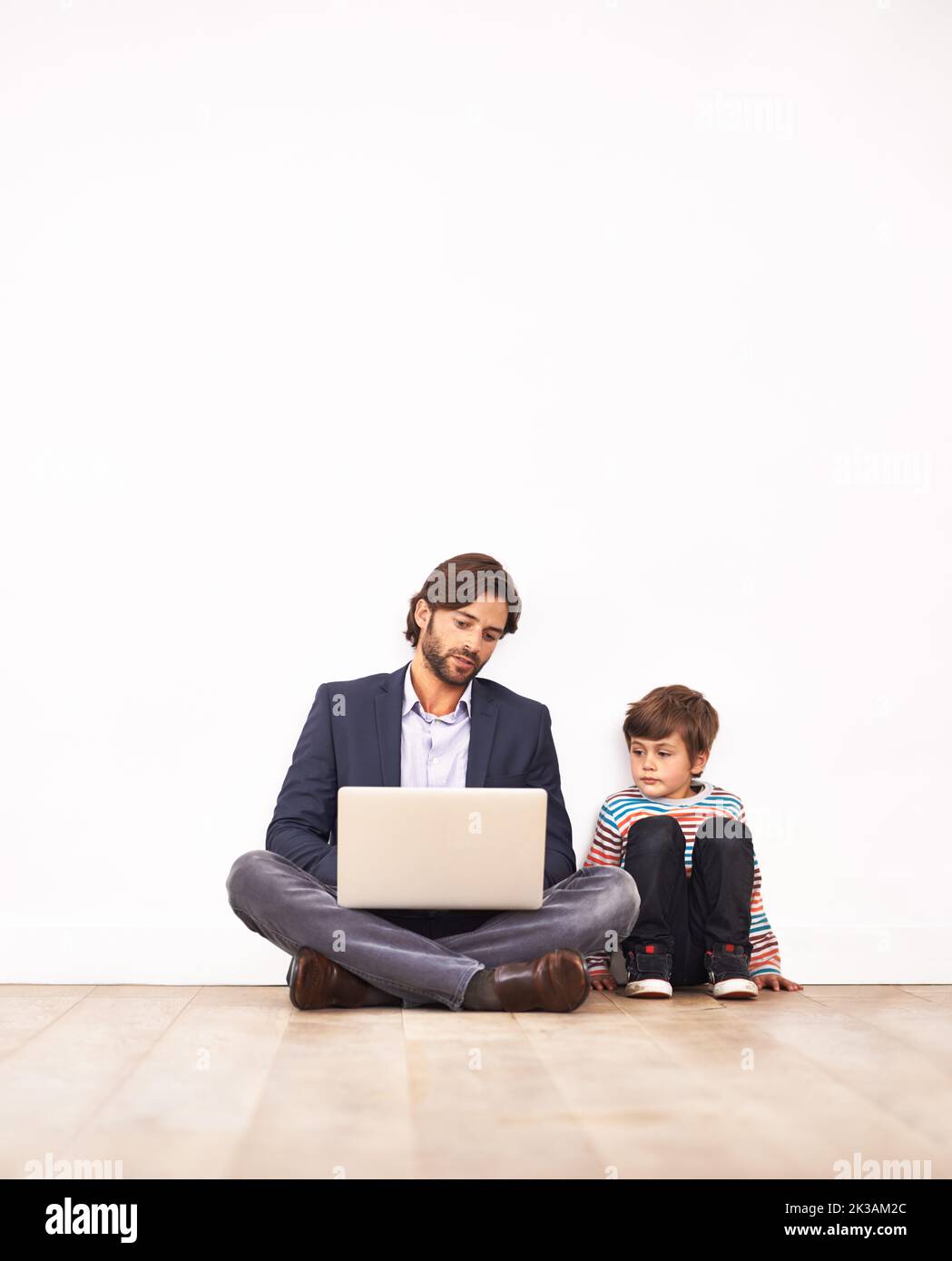 Genitorialità moderna. Un padre e suo figlio, seduti sul pavimento e guardando un portatile insieme. Foto Stock