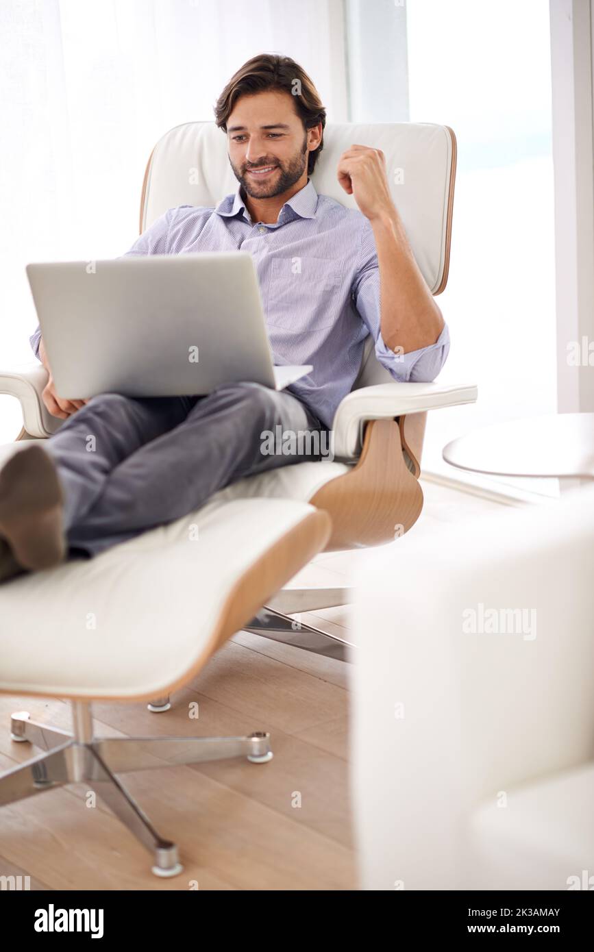 Mescolando affari e piacere. Un bel uomo d'affari che si rilassa mentre lavora sul suo laptop. Foto Stock