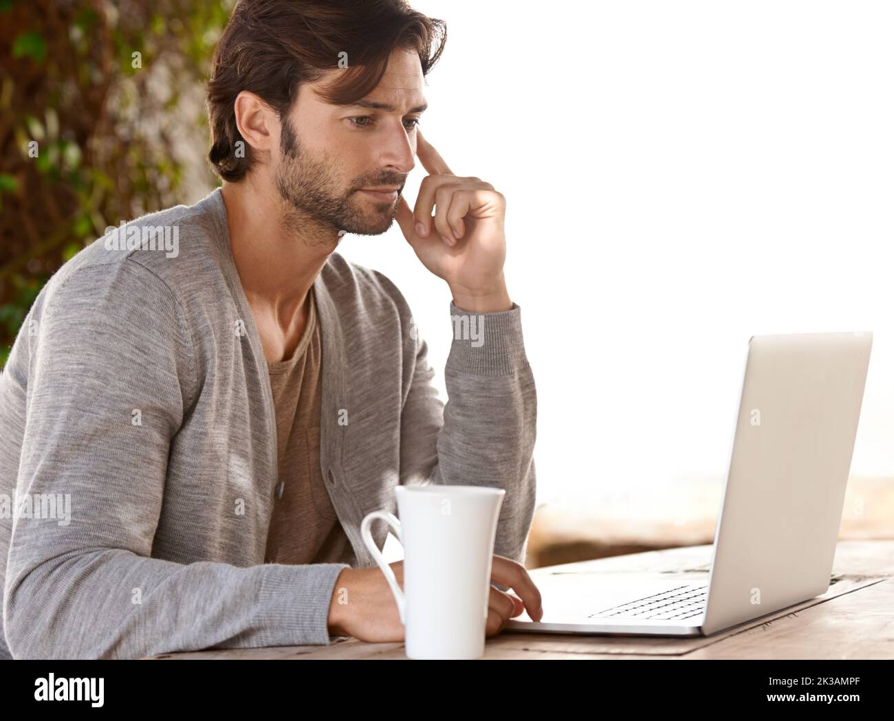 Profondo nel pensiero online. Un bel giovane uomo che lavora sul suo laptop all'esterno. Foto Stock