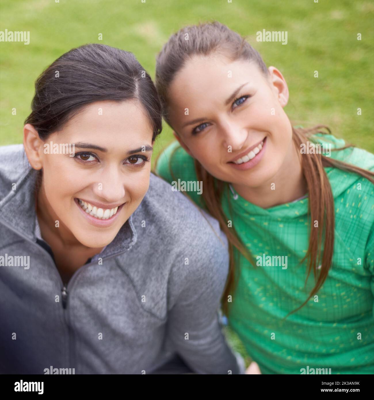 Giovane, in forma e con grande sensazione. Ritratto di due giovani donne in abbigliamento sportivo seduto su un campo sportivo erboso. Foto Stock