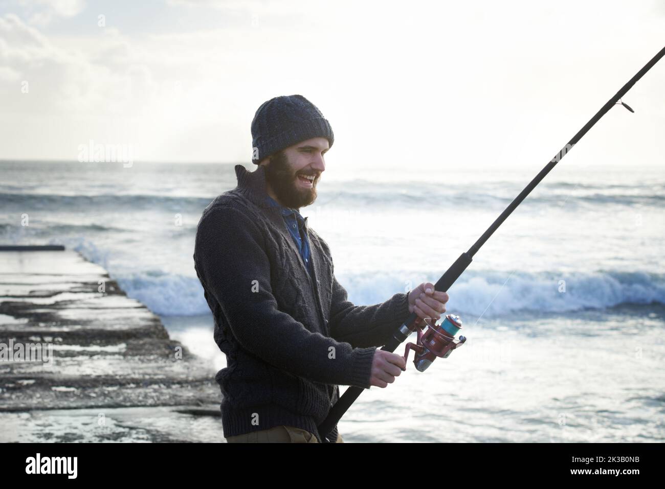 Prendendosi il suo tempo per la grande cattura. Un pescatore da solo che pesca fuori da un molo all'oceano. Foto Stock